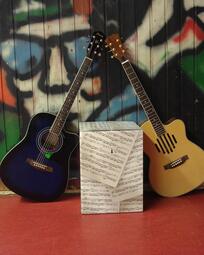 Vergrößerte Ansicht von Foto von zwei Gitarren, die an einer Wand und neben einem Papphocker aus Notenpapier stehen