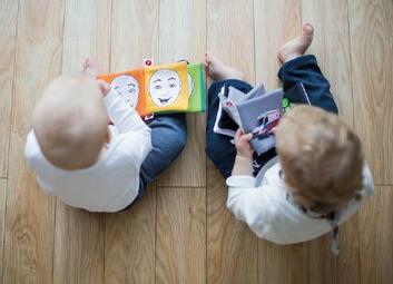 Vergrößerte Ansicht von Zwei Kleinkinder sitzen auf einem Holzboden und schauen sich Bilderbücher an