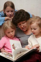 Vergrößerte Ansicht von Foto einer Vorlesepatin, die drei Kindern aus einem Buch vorliest
