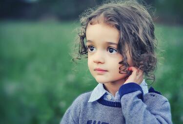 Vergrößerte Ansicht von Portraitfoto von einem Kind, das auf einer Wiese steht und in die Ferne schaut 