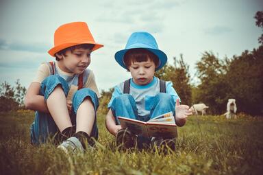 Vergrößerte Ansicht von Zwei Jungen sitzen auf einer Wiese und lesen ein Buch