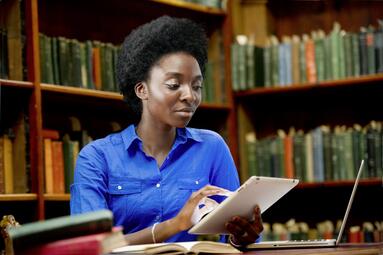 Vergrößerte Ansicht von Eine Frau sitzt mit einem Tablet in Händen in einer Bibliothek