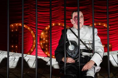 Vergrößerte Ansicht von Matthias Breitenbach sitzt und hält seine pickelhaube im Arm. Er blickt gedankenverloren durch die Gitterstäbe vor ihm.