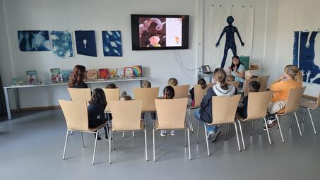 Vergrößerte Ansicht von Kinder betrachten ein Bilderbuchkino auf einem großen Fernseher.