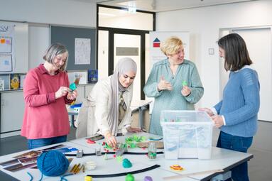 Vergrößerte Ansicht von Vier Frauen stehen um einen Tisch mit Bastelmaterialien herum. Sie reden und lachen zusammen.