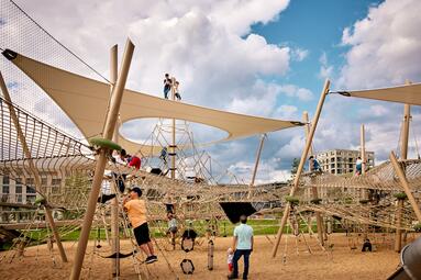 Vergrößerte Ansicht von Ein Spielplatz mit Holzpfählen, dazwischen Netze, darüber ein Sonnensegel. Kinder Spielen in der Spielstation &quot;Vernetzung&quot; in der Parkschale Käfertal, Spinelli-Park, Mannheim