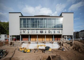 Vergrößerte Ansicht von Seitenansicht auf das Spielhaus am Goetheplatz. Vor dem Gebäude befindet sich ein Graben mit gelben Baustellenfahrzeugen.