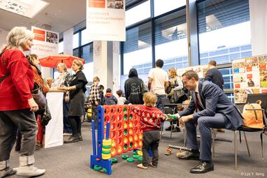 Vergrößerte Ansicht von Ein Überblick über den Stand. Im Vordergrund befindet sich ein Vier Gewinnt, das ein Kind mit seinem Vater spielt.