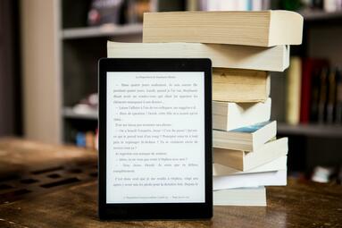 Vergrößerte Ansicht von E-Book-Reader vor Bücherstapel