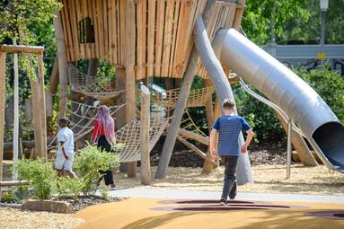 Vergrößerte Ansicht von Mehrgenerationenspielplatz Rheinau: Drei Kinder vor einem großen Klettergerüst mit Tunnelrutsche