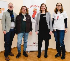 Vergrößerte Ansicht von Bürgermeister Grunert, Markus Altmeyer, Christine Wieder und Bettina Harling stehen lächelnd nebeneinander. Im Hintergrund ist das Feuergriffel-Symbol zu sehen.