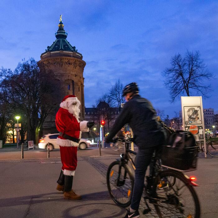 Vor dem Mannheimer Wasserturm übergibt ein Nikolaus Geschenke an einen Radfahrer.